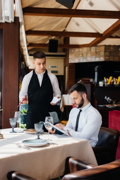 A young businessman in a fine restaurant examines the menu and makes an order to a young waiter in a stylish apron. Customer service.