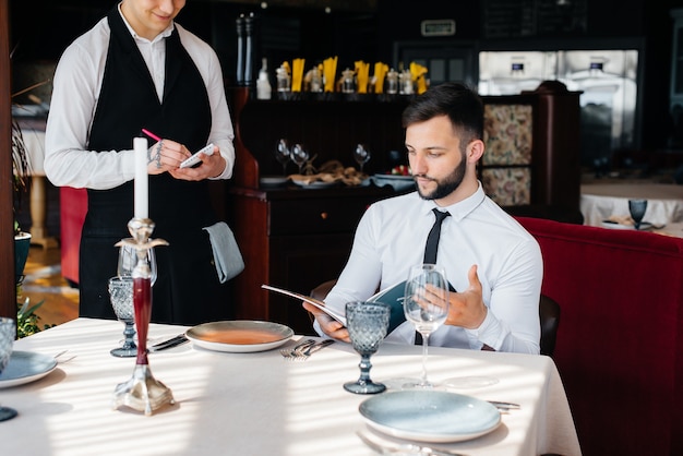 Un giovane uomo d'affari in un raffinato ristorante esamina il menu e fa un ordine a un giovane cameriere con un elegante grembiule. assistenza clienti.