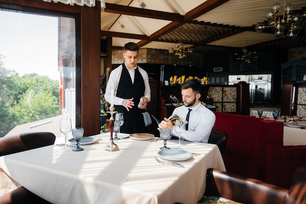 A young businessman in a fine restaurant examines the menu and\
makes an order to a young waiter in a stylish apron. customer\
service.