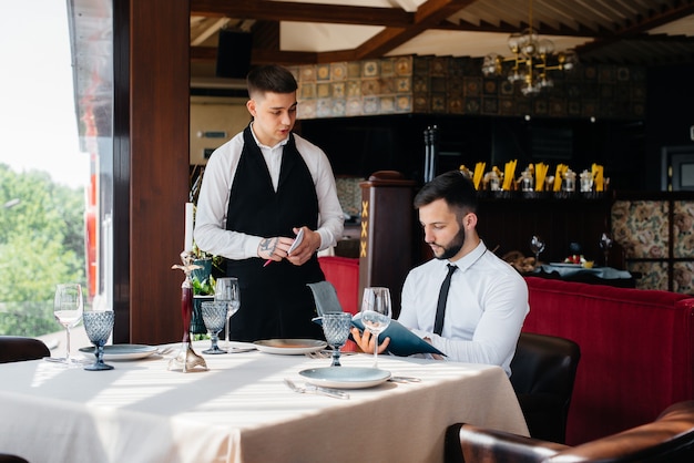 A young businessman in a fine restaurant examines the menu and\
makes an order to a young waiter in a stylish apron. customer\
service.