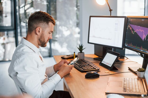 Young businessman in formal clothes is in office with multiple screens Conception of exchange