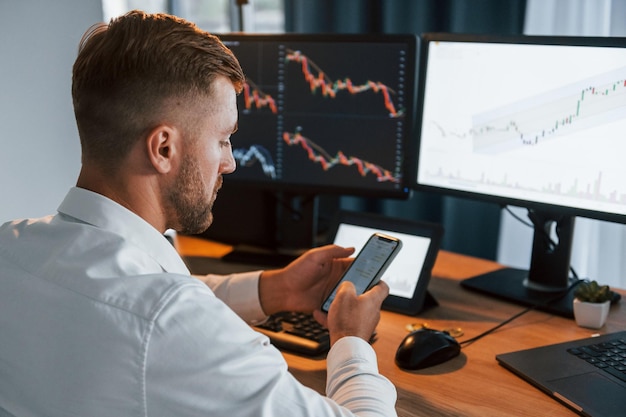 Young businessman in formal clothes is in office with multiple screens Conception of exchange