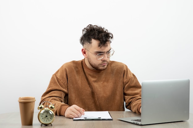 Young businessman in glasses sitting on his desk and working on laptop. 