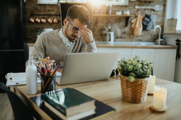 Young businessman having a headache while working on a computer at home