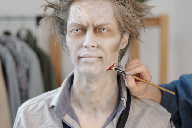 Young businessman having zombie makeup applied on his face in studio