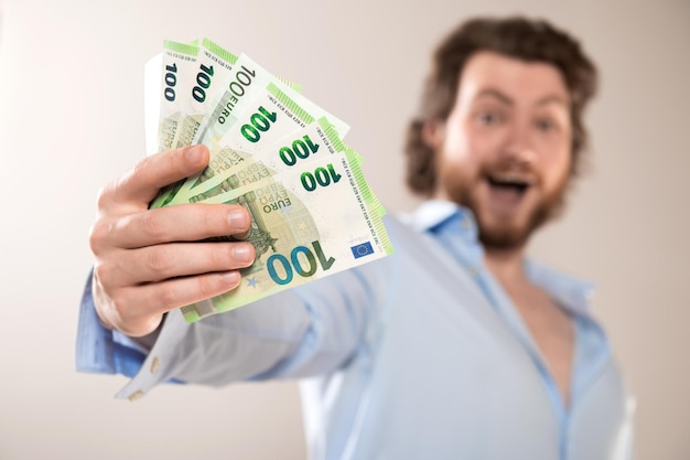 Фото Молодой бизнесмен держит 100 евро наличные банкноты изолированы на сером фоне сосредоточиться на деньгах