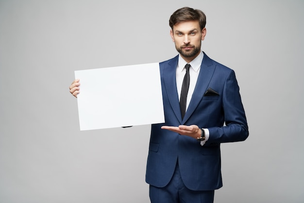 Young businessman holding blank sign over grey wall