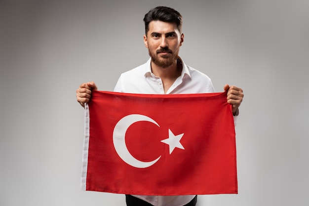 Young businessman holding a flag of Turkey on gray background