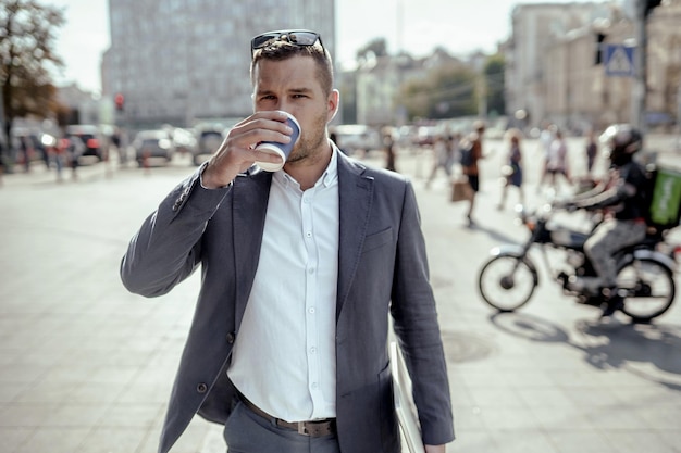 写真 コーヒーを飲みながら彼のラップトップを保持している青年実業家。通りに立っています。