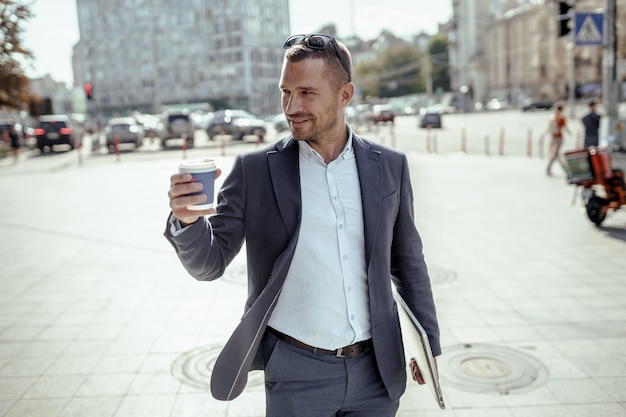 Giovane uomo d'affari che tiene il suo computer portatile mentre beve caffè. in piedi per strada.