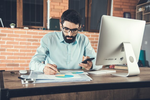 Young businessman holding smart phone and working in office