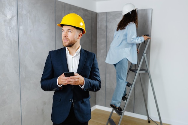 A young businessman holds a phone in his hands and checks the work of a designer in creating an interior in a room The concept of repair on a modern design