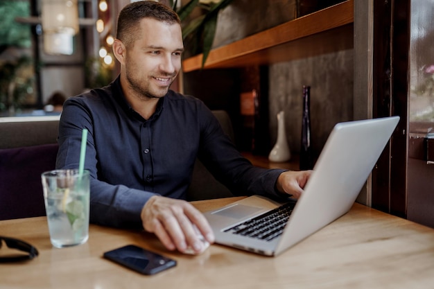 Young businessman is having online meeting on laptop in restaurant. Remote work.