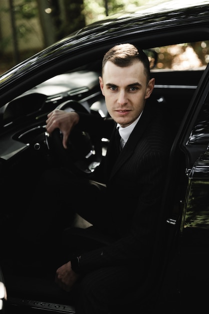 Young businessman is sitting in an expensive car and looking at the camera. the groom is driving. business man. successful guy. rich man.