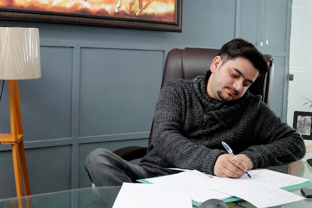 A young businessman is sitting in the office and writing something on paper.