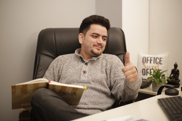 A young businessman is watching in computer and showing thumbs up sign.