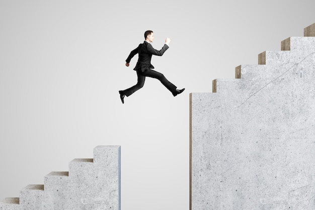 Фото Молодой бизнесмен прыгает по лестнице на сером фоне концепция успеха и роста
