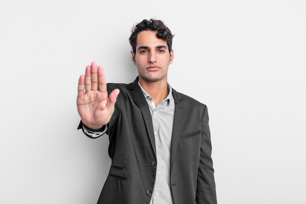 Young businessman looking serious, stern, displeased and angry showing open palm making stop gesture