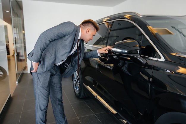 A young businessman looks at a new car in a car dealership