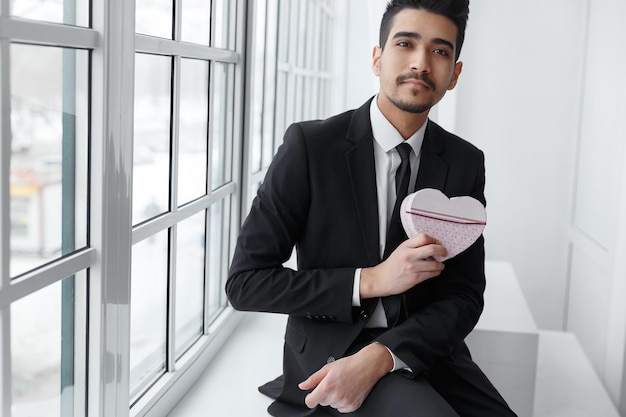 Young businessman in love sitting on windowsill