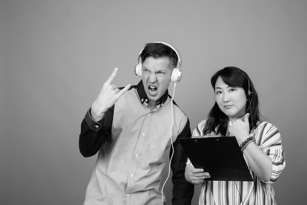 Young businessman and mature Japanese businesswoman together against gray in black and white