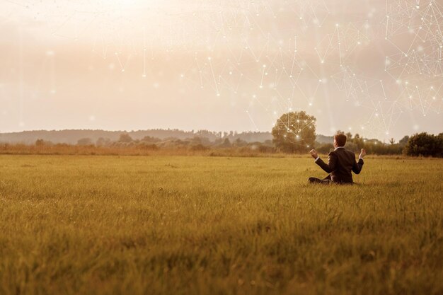 Young businessman meditates in a field on the Internet