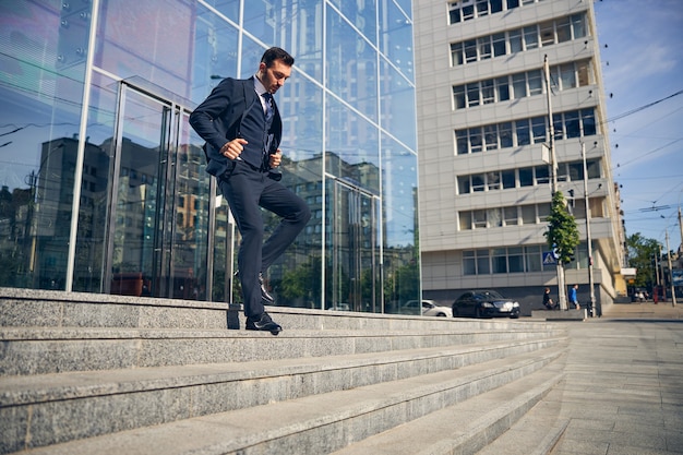 Young businessman in official clothes leaving beautiful business center made of glass and hurrying