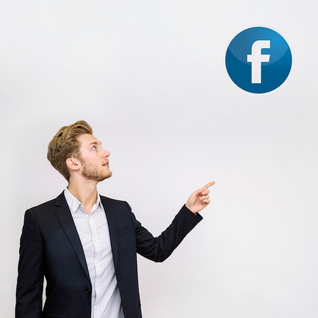 Foto giovane uomo d'affari che punta all'icona di facebook sul muro