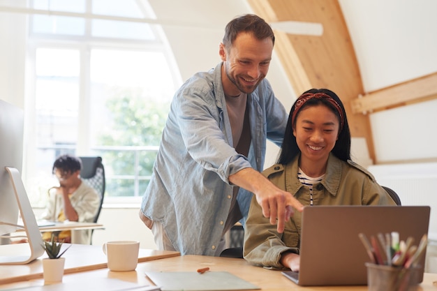 Young businessman pointing at monitor of laptop and discussing business presentation together with his colleague at office