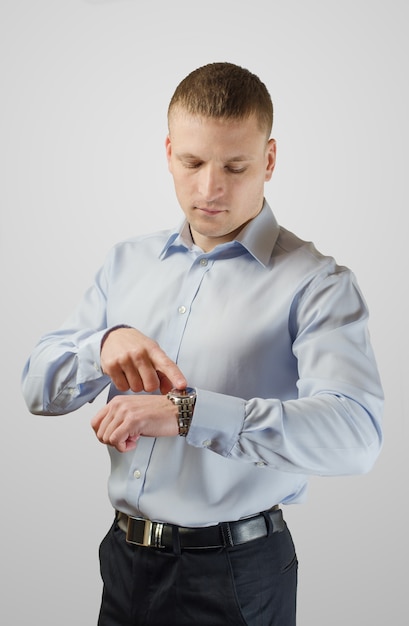Young businessman points to his watch on his arm. Isolated on white surface.