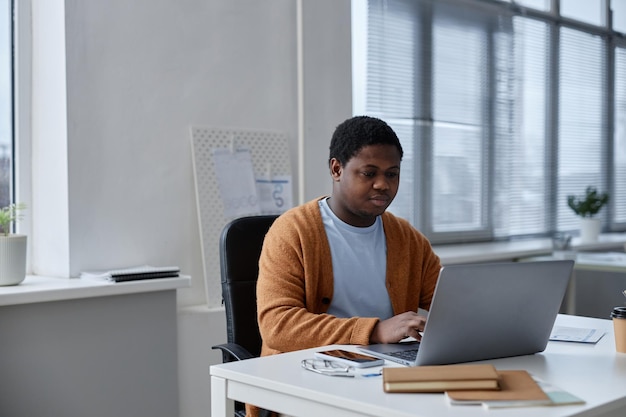 Young businessman sitting by desk looking at laptop screen and typing