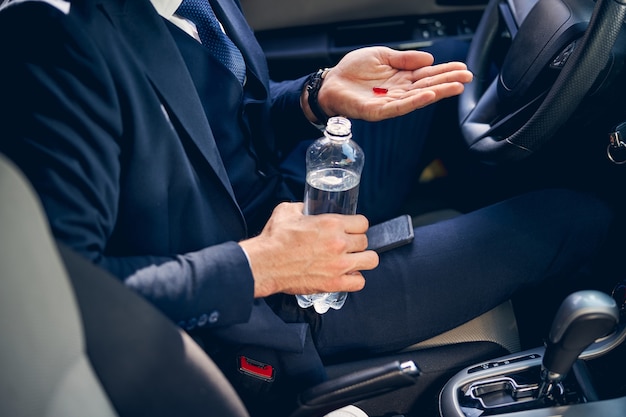 Young businessman sitting in his car and taking medicine while having headache