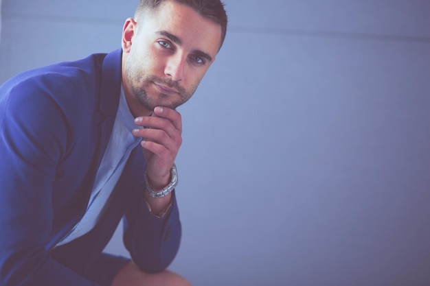 Young businessman sitting isolated on grey background