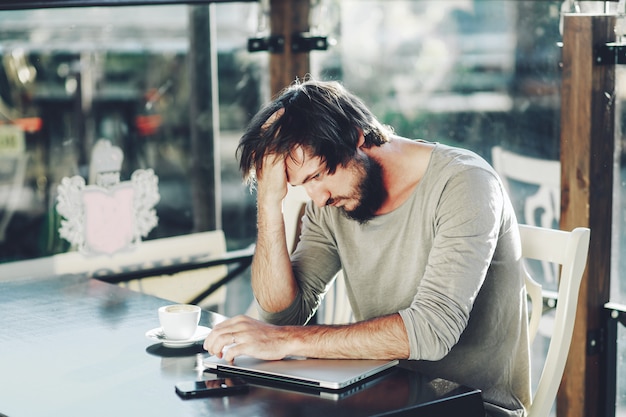 Young businessman sitting outside corporate office holding head with hands looking down. Negative human emotion facial expression feelings.