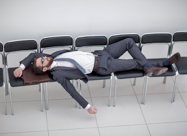 Young businessman sleeping on chairs in the office hallwaythe\
concept of waiting