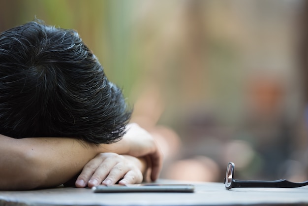 Young businessman sleeping on desk with smartphone and glasses.