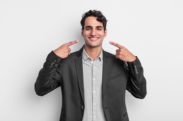 Young businessman smiling confidently pointing to own broad smile, positive, relaxed, satisfied attitude