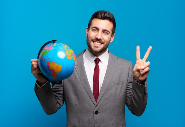 Young businessman smiling and looking friendly, showing number two or second with hand forward, counting down holding a world globe map