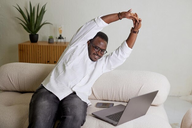 Young businessman stretching his arms with a laptop in a cozy home