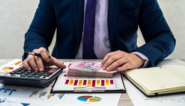 Young businessman in suit counts hryvnia money and works with charts and documents as net monthly income