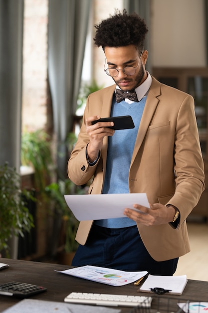 Young businessman in suit photographing documents on mobile phone for sending