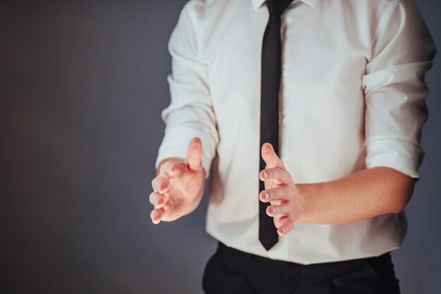 Il giovane uomo d'affari in un vestito mostra la sua mano su uno sfondo scuro isolato