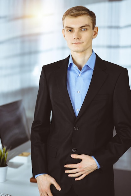 Young businessman in a suit, while standing in a sunny office. Business success concept nowadays.