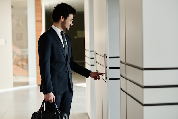 사무실 건물 복도에 서 있는 엘리베이터를 사용하여 서류 가방을 들고 정장을 입은 젊은 사업가