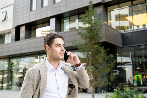 Молодой бизнесмен разговаривает по мобильному телефону во время прогулки по улице города