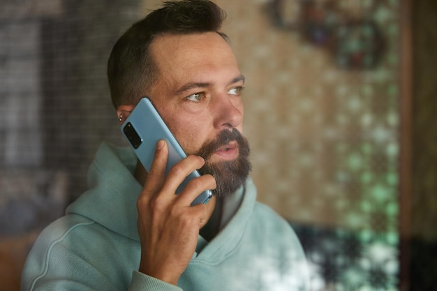 Young businessman talking on his phone indoor through glass bearded man in casual clothes using his