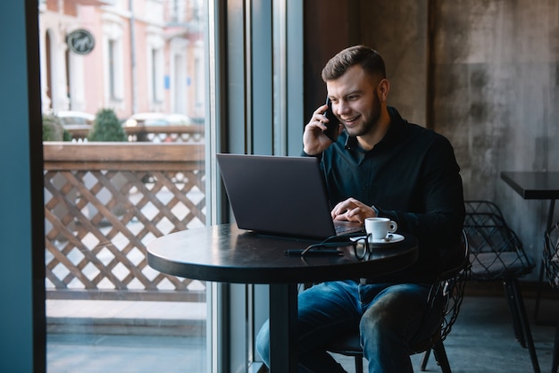 Young businessman talking on mobile phone while working on laptop in cafe