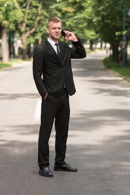 Young Businessman Talking On The Phone While Standing Outside In ParkxA