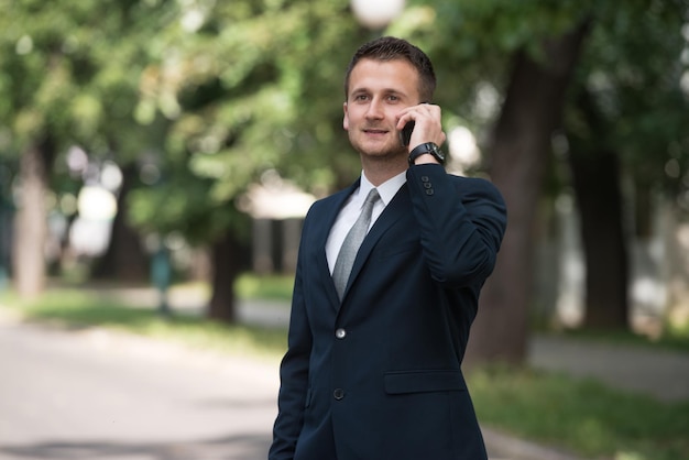 Giovane uomo d'affari che parla al telefono mentre si trova fuori in parkxa