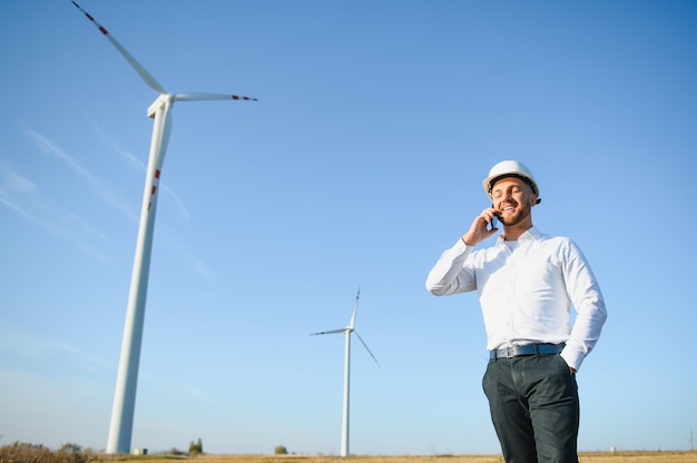 風力タービンフィールド、グリーンエネルギーの概念でスマートフォンを使用してマネージャーと話す若いビジネスマン